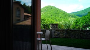 Un balcón con un muro de piedra, una silla y vistas a un valle verde y montañas.