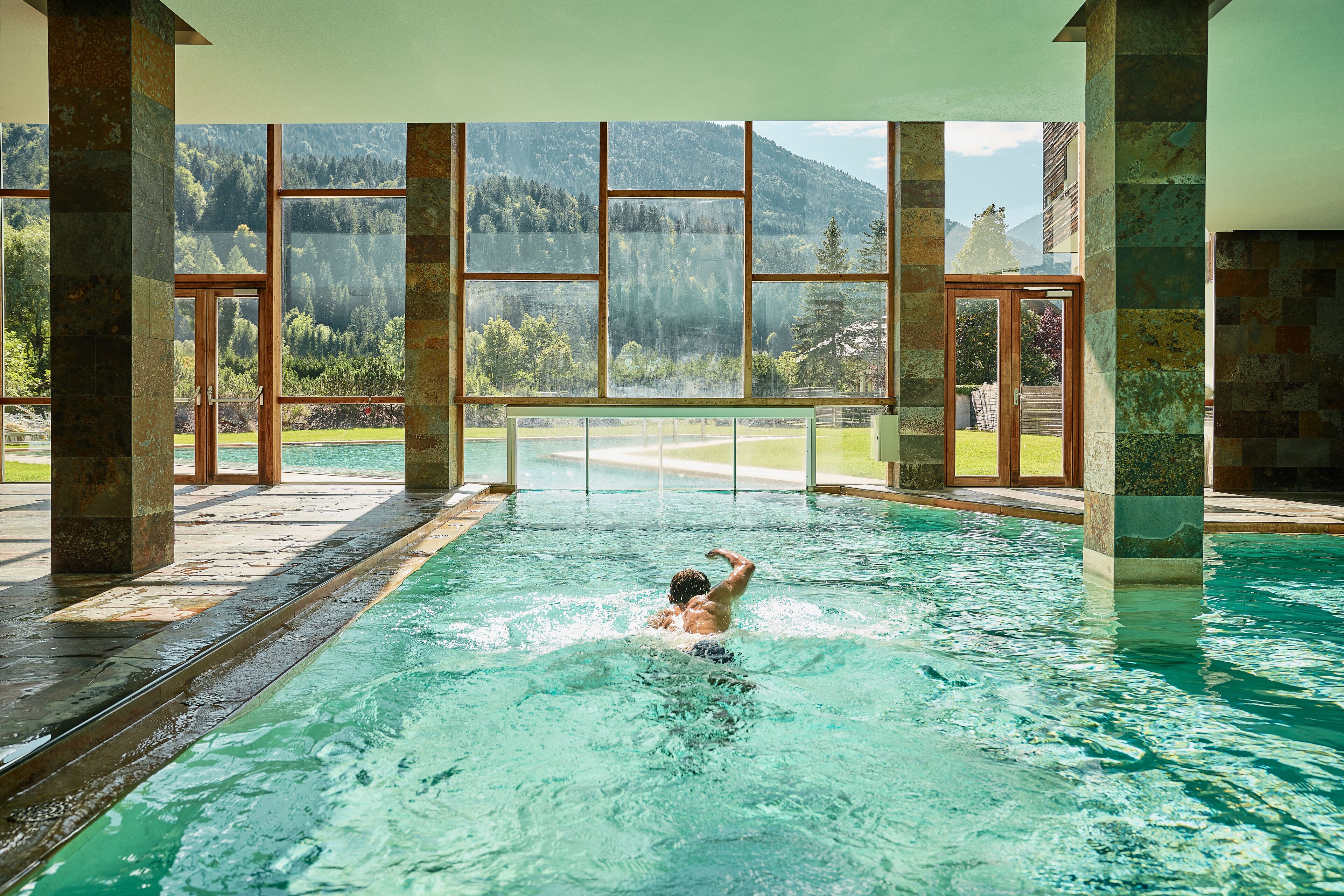 Ein Schwimmbad mit Blick auf Berge und Bäume durch große Fenster.