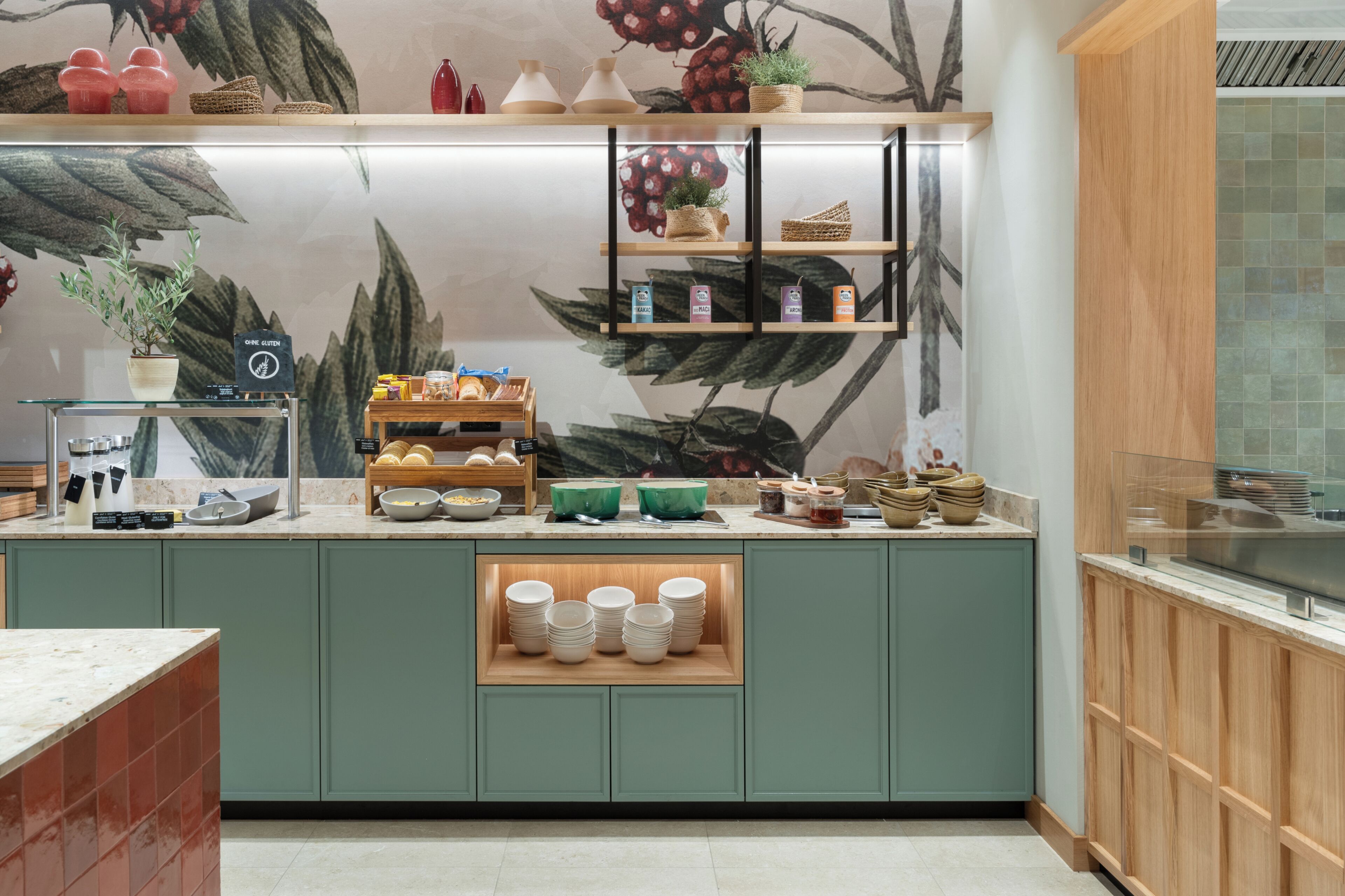 Une cuisine avec des armoires vertes, un comptoir en bois et une fresque murale sur le thème des fruits.