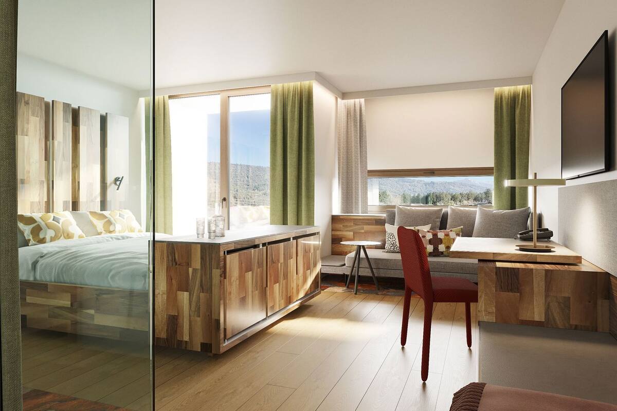 Habitación de hotel moderna con cama, escritorio, silla, televisor y vistas a las montañas.