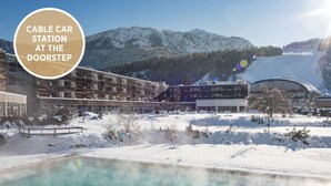 Ein modernes Gebäude mit Pool, umgeben von schneebedeckten Bergen und einer Skipiste.