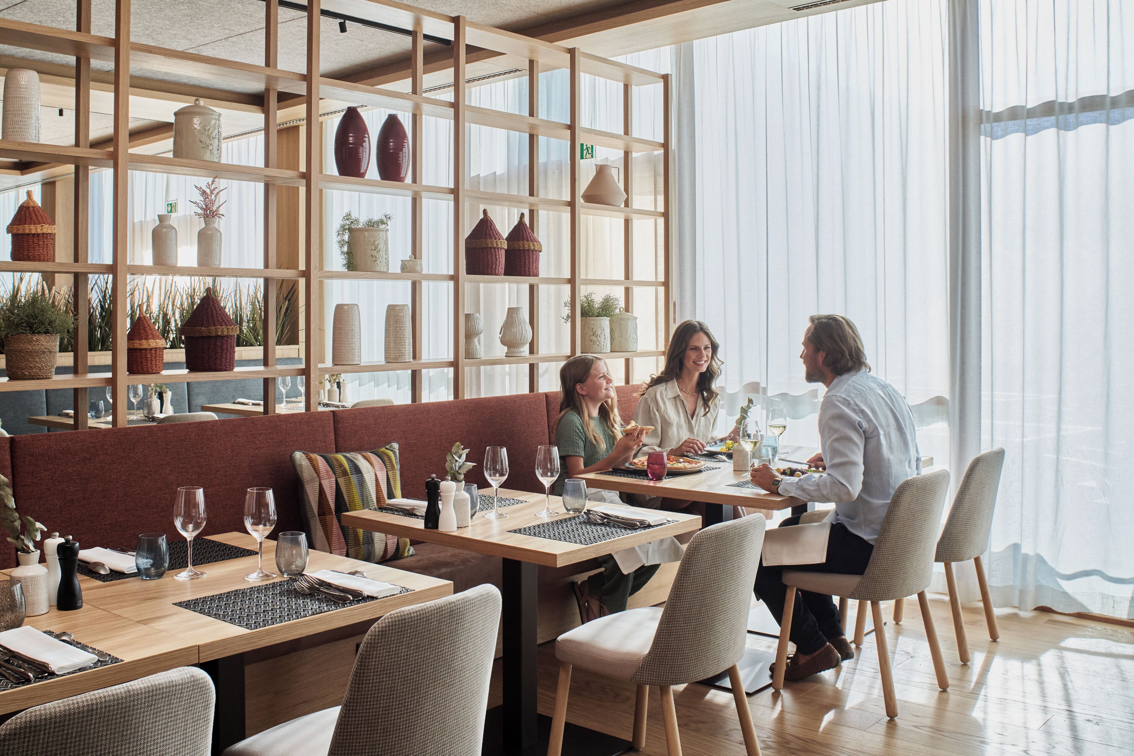 Un restaurante con mesas de madera, asientos acolchados y estantes con adornos.