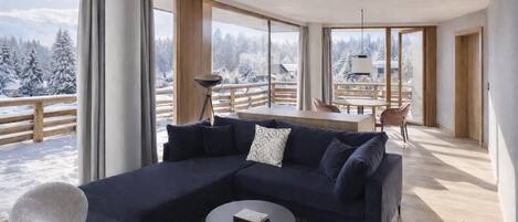 Una sala de estar moderna con un sofá seccional azul oscuro, una mesa redonda y vistas a un paisaje nevado a través de amplios ventanales.