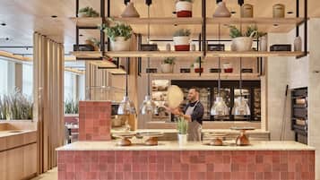 Una cuina moderna amb prestatges de fusta que contenen plantes i estris de cuina, una persona preparant menjar, i una màquina de cafè al fons.