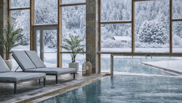Ein Poolbereich mit Liegestühlen und großen Fenstern mit Blick auf einen verschneiten Wald.