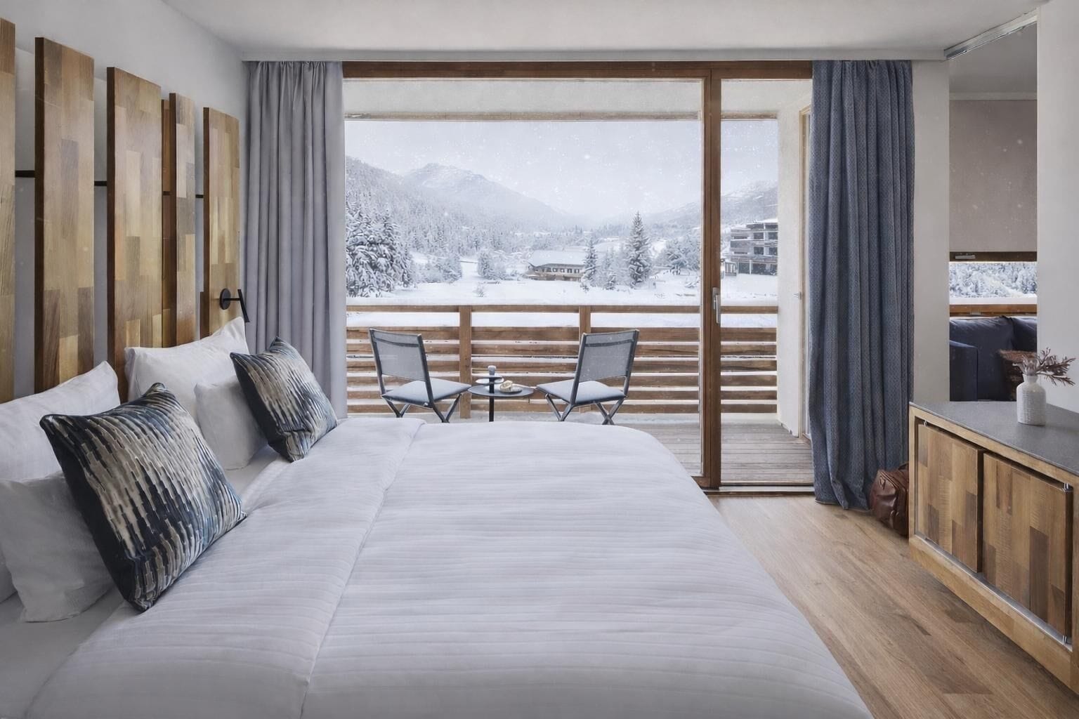 Ein Schlafzimmer mit einem großen Bett, zwei Stühlen, einem kleinen Tisch und einem Balkon mit Blick auf schneebedeckte Berge.
