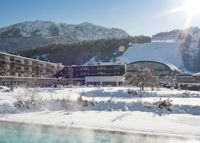 Un edificio moderno con piscina, rodeado de montañas nevadas y una pista de esquí.