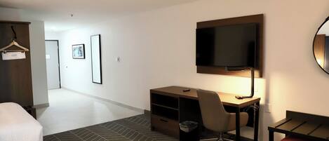 A hotel room with a bed, a desk with a chair, a television, and a wardrobe.