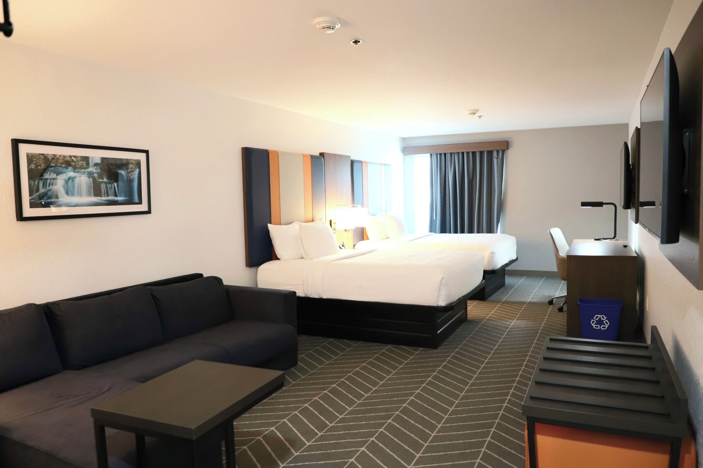 A hotel room with a bed, a sofa, a desk, a TV, and a picture on the wall.