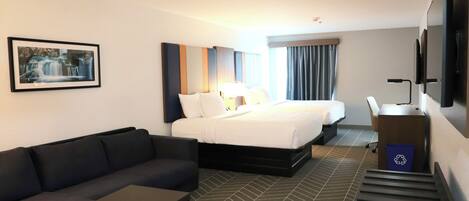 A hotel room with a bed, a sofa, a desk, a TV, and a picture on the wall.