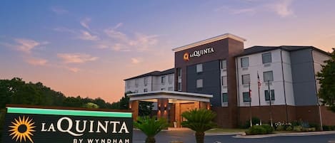 A hotel sign with 'LA QUINTA BY WYNDHAM' and a modern building with multiple windows and a flag.