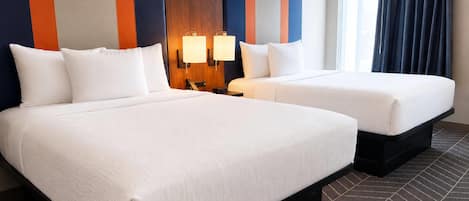 A hotel room with two beds, a wooden headboard, a nightstand, a lamp, and a window with curtains.
