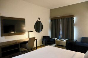 A hotel room with a bed, a desk, a chair, a TV, a mirror, and a window with curtains.