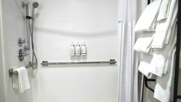 Área de chuveiro com chuveiro manual, torneira fixa na parede e porta-toalhas com toalhas dobradas.