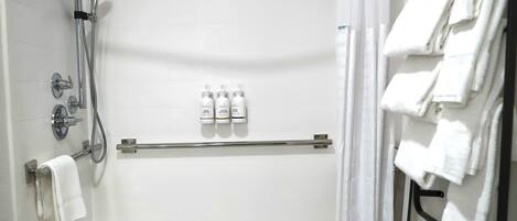 A shower area with a handheld showerhead, a wall-mounted faucet, and a towel rack with folded towels.