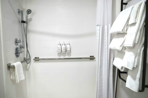 A shower area with a handheld showerhead, a wall-mounted faucet, and a towel rack with folded towels.