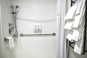 Zona de ducha con cabezal de ducha de mano, grifo empotrado en la pared y toallero con toallas dobladas.