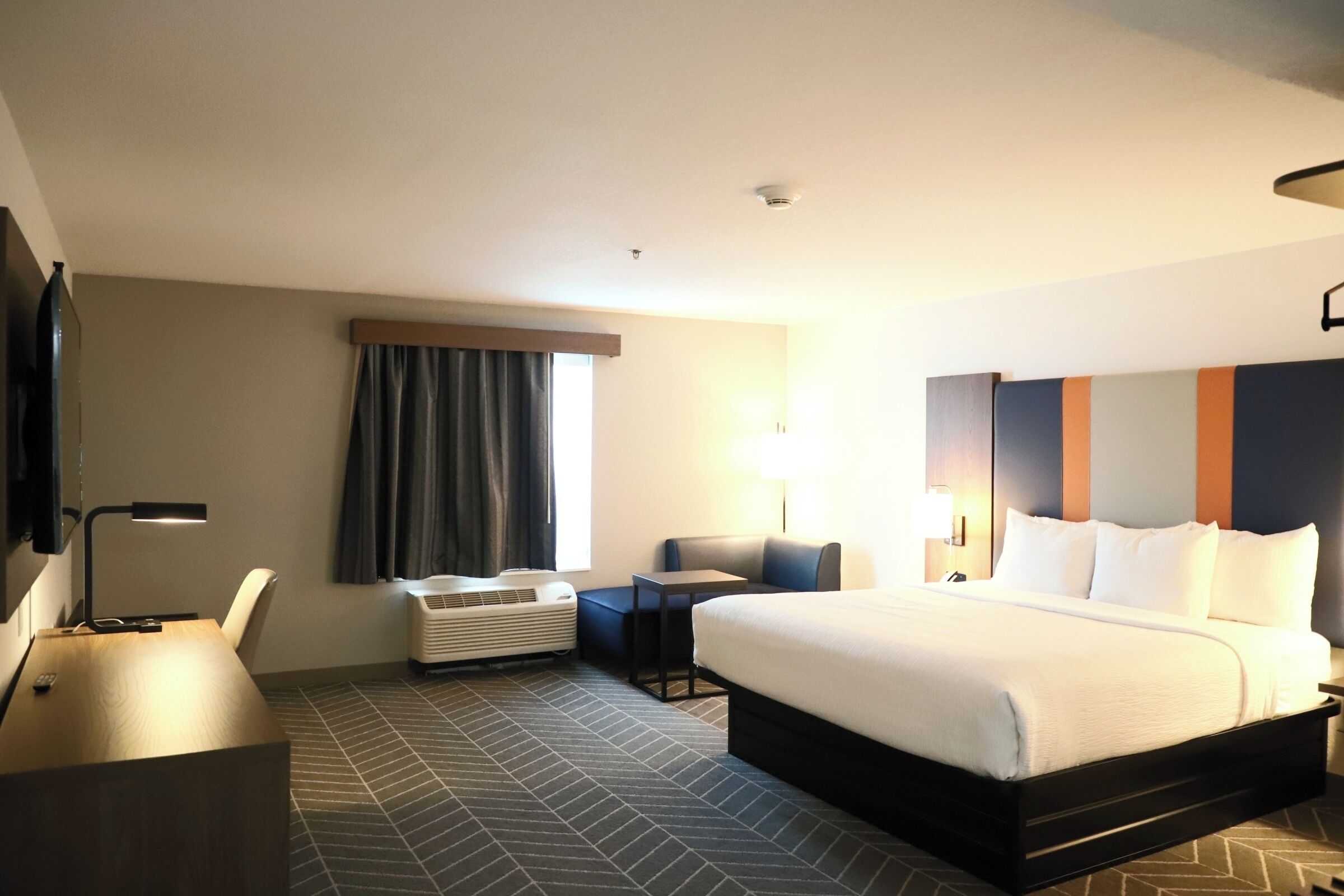 Habitación de hotel con cama, escritorio, silla, televisión y ventana con cortinas.