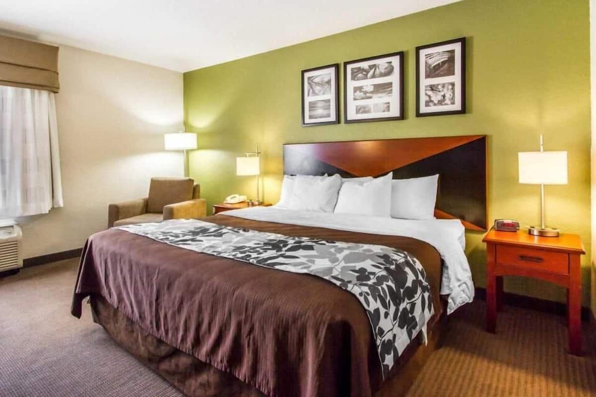 A hotel room with a large bed, two bedside tables, a chair, and a wall with three framed pictures.