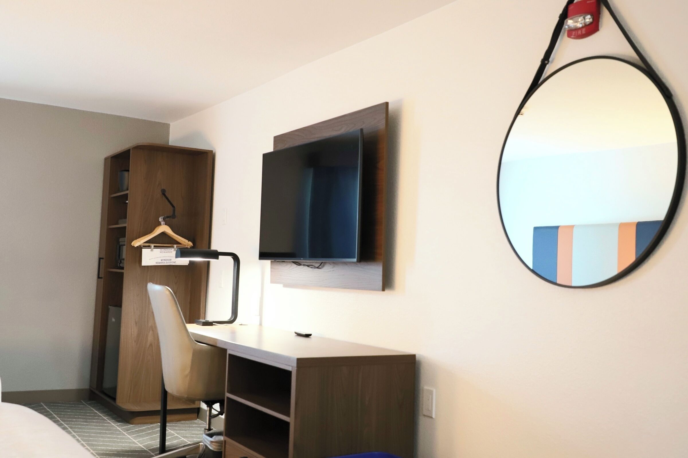 A hotel room with a desk, chair, TV, wardrobe, and a mirror.