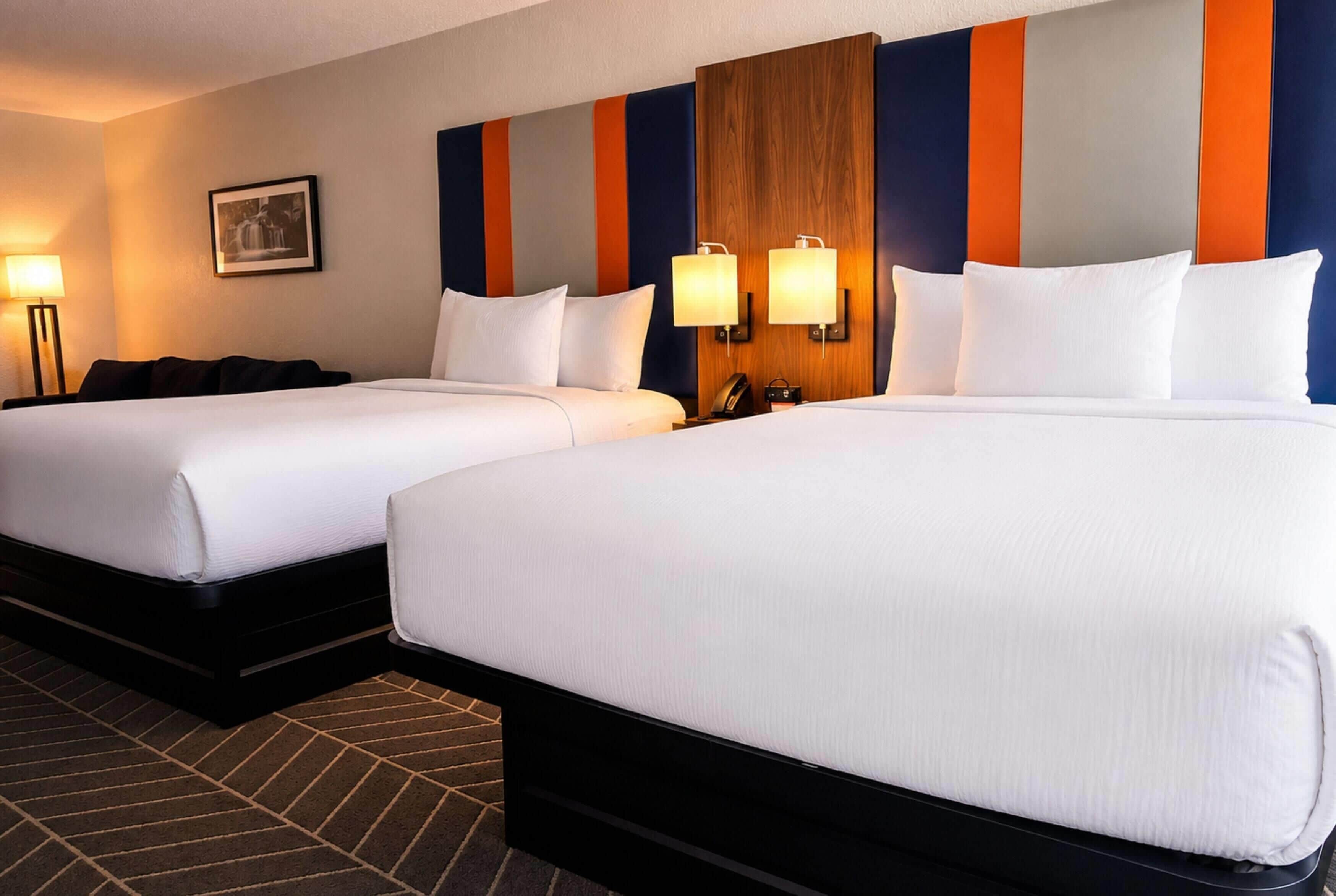 A hotel room with two beds, a wall-mounted lamp, and a framed picture.
