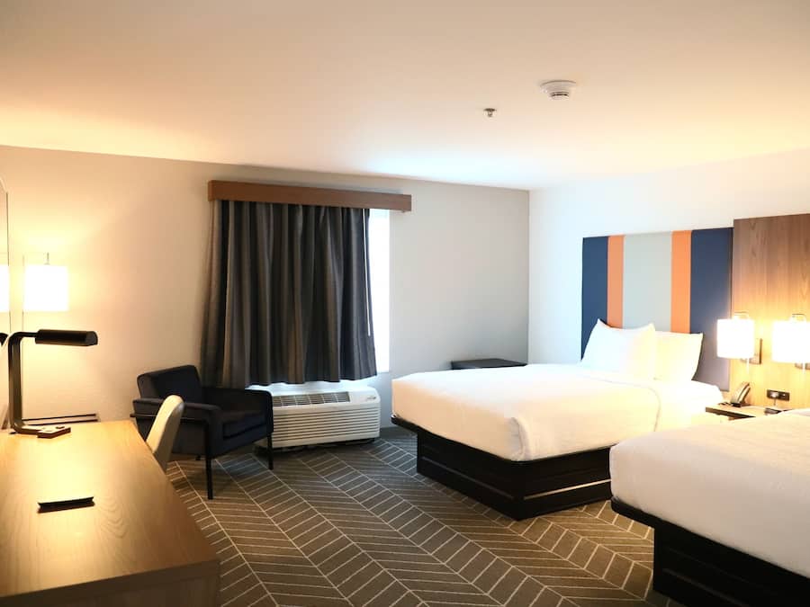 A hotel room with a bed, a desk, a chair, a heater, and a window with curtains.