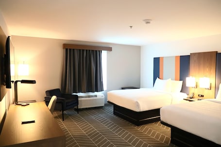 A hotel room with a bed, a desk, a chair, a heater, and a window with curtains.