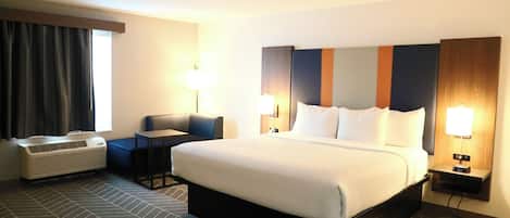 A hotel room with a bed, a desk, a chair, a heater, and a window with curtains.