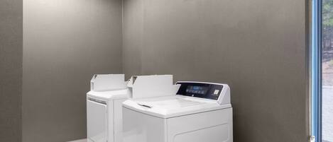 A laundry room with two white front-loading washing machines and a large window on the right.