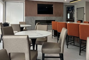 A modern interior with round tables and chairs, a flat-screen TV mounted on a wall, and a bar area with orange chairs.