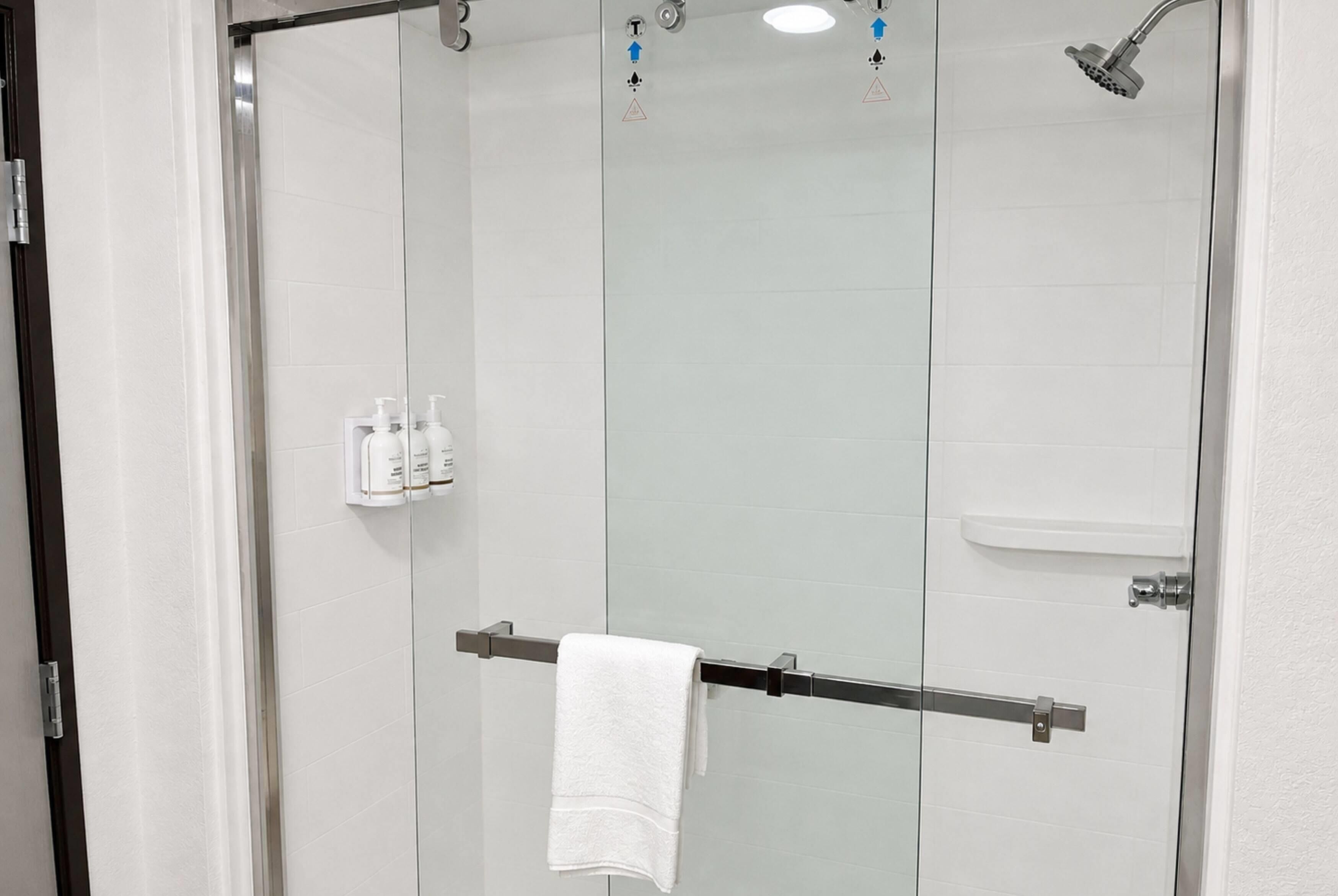 Une cabine de douche fermée par des parois en verre, dotée d’un porte-serviettes et d’un panneau de commande avec des symboles de sécurité, ainsi que d’un mur recouvert de carreaux blancs.