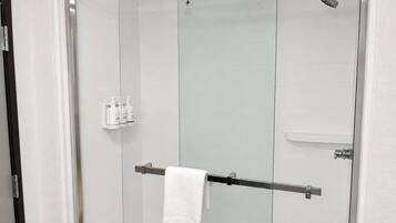 Une cabine de douche fermée par des parois en verre, dotée d’un porte-serviettes et d’un panneau de commande avec des symboles de sécurité, ainsi que d’un mur recouvert de carreaux blancs.
