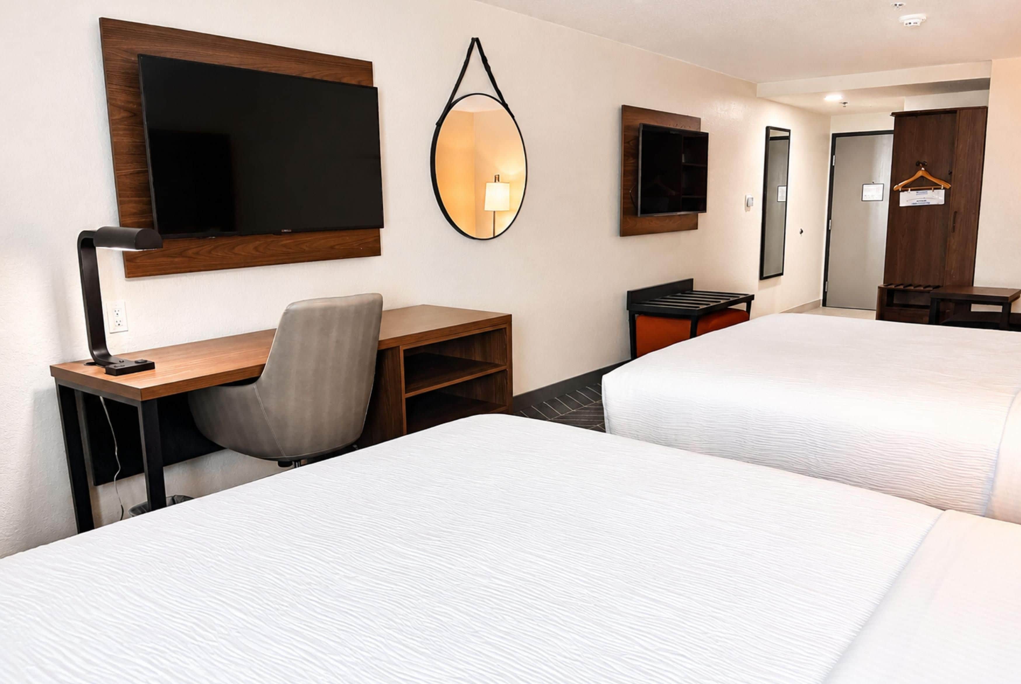A hotel room with two beds, a desk, a chair, a TV, and a mirror.