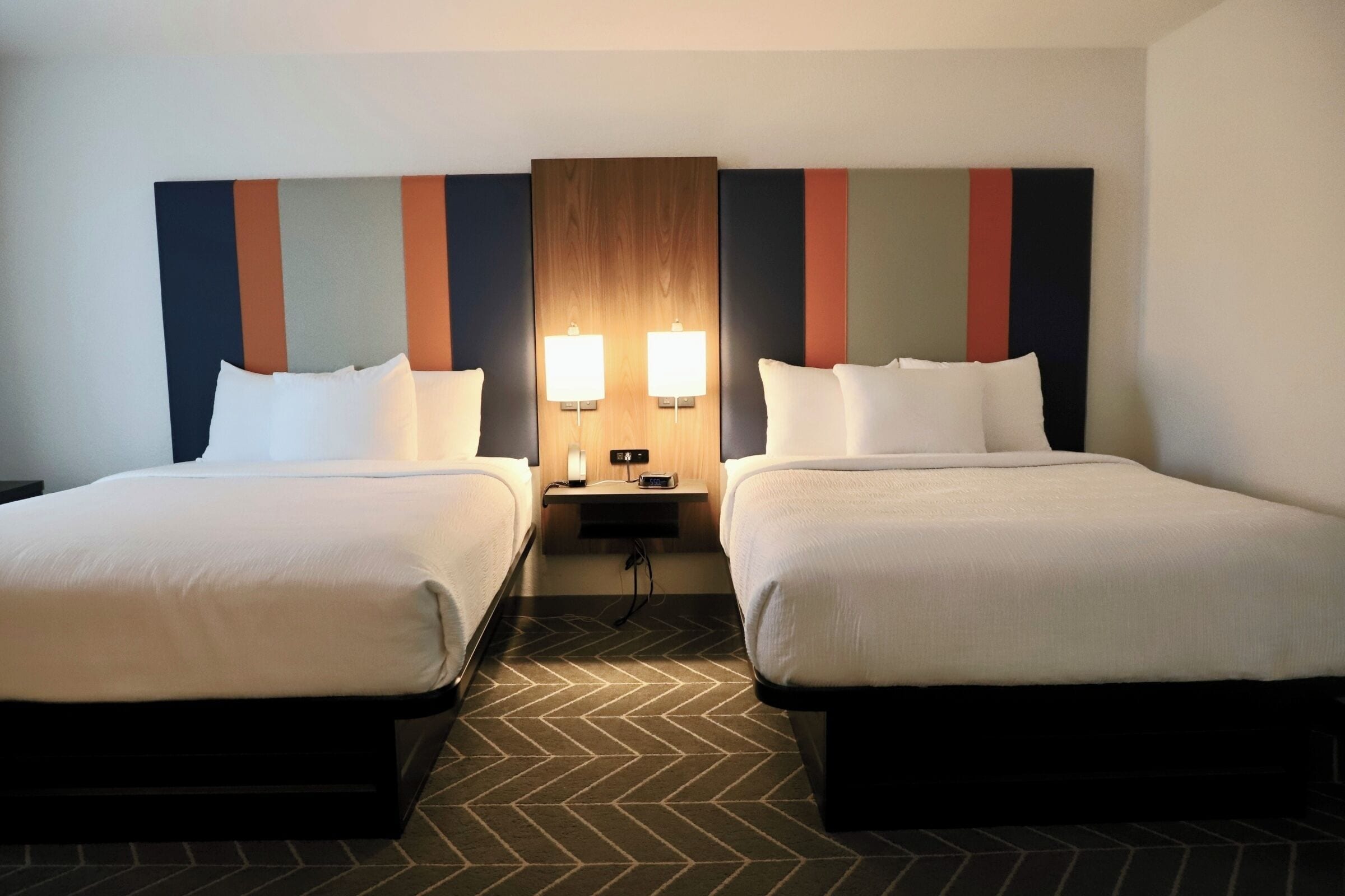 Ein Hotelzimmer mit zwei Betten, einem Nachttisch mit Lampen und einem hölzernen Kopfteil.