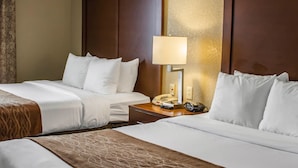 A hotel room with two beds, a bedside table with a lamp, a telephone, and a wall-mounted light fixture.