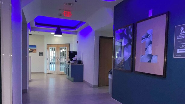 A hallway with a reception desk, framed artwork on the wall, and a blue-lit ceiling.