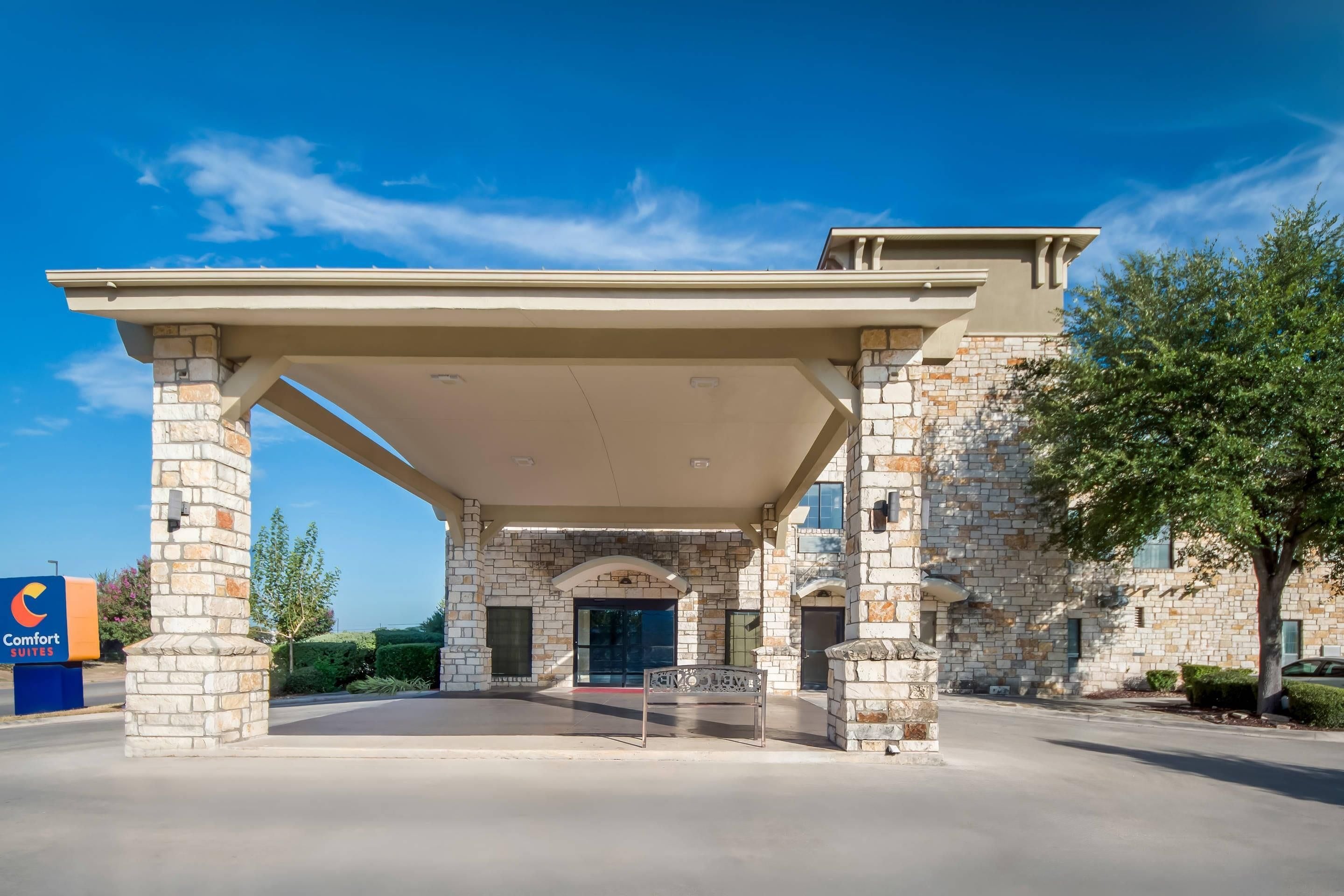 A hotel entrance with a covered patio, stone facade, and a sign indicating 'Comfort Suites.'