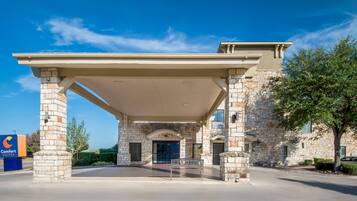 A hotel entrance with a covered patio, stone facade, and a sign indicating 'Comfort Suites.'