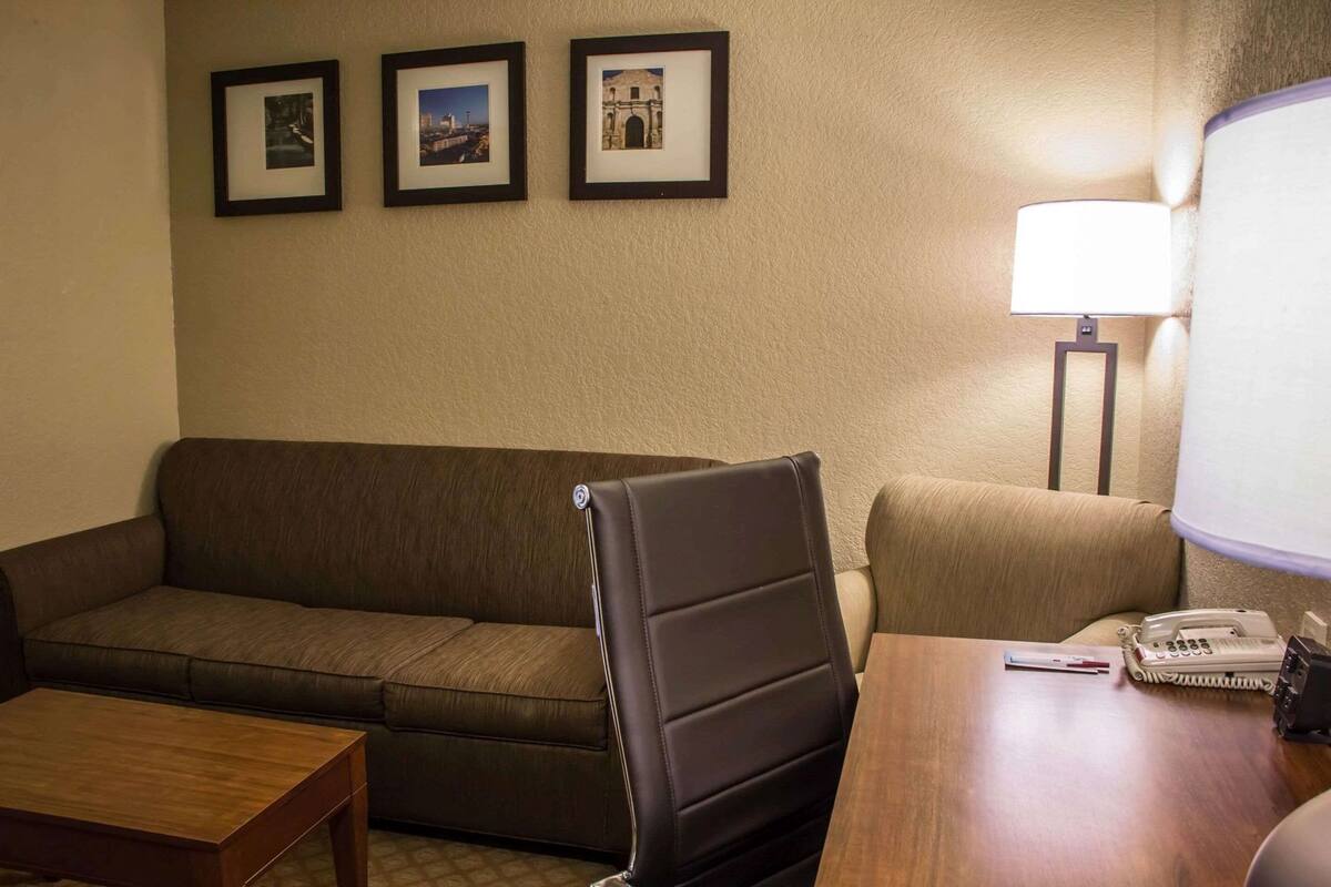 Une chambre d’hôtel avec un canapé en cuir marron, une table basse en bois, un bureau avec un téléphone et trois tableaux encadrés accrochés au mur.