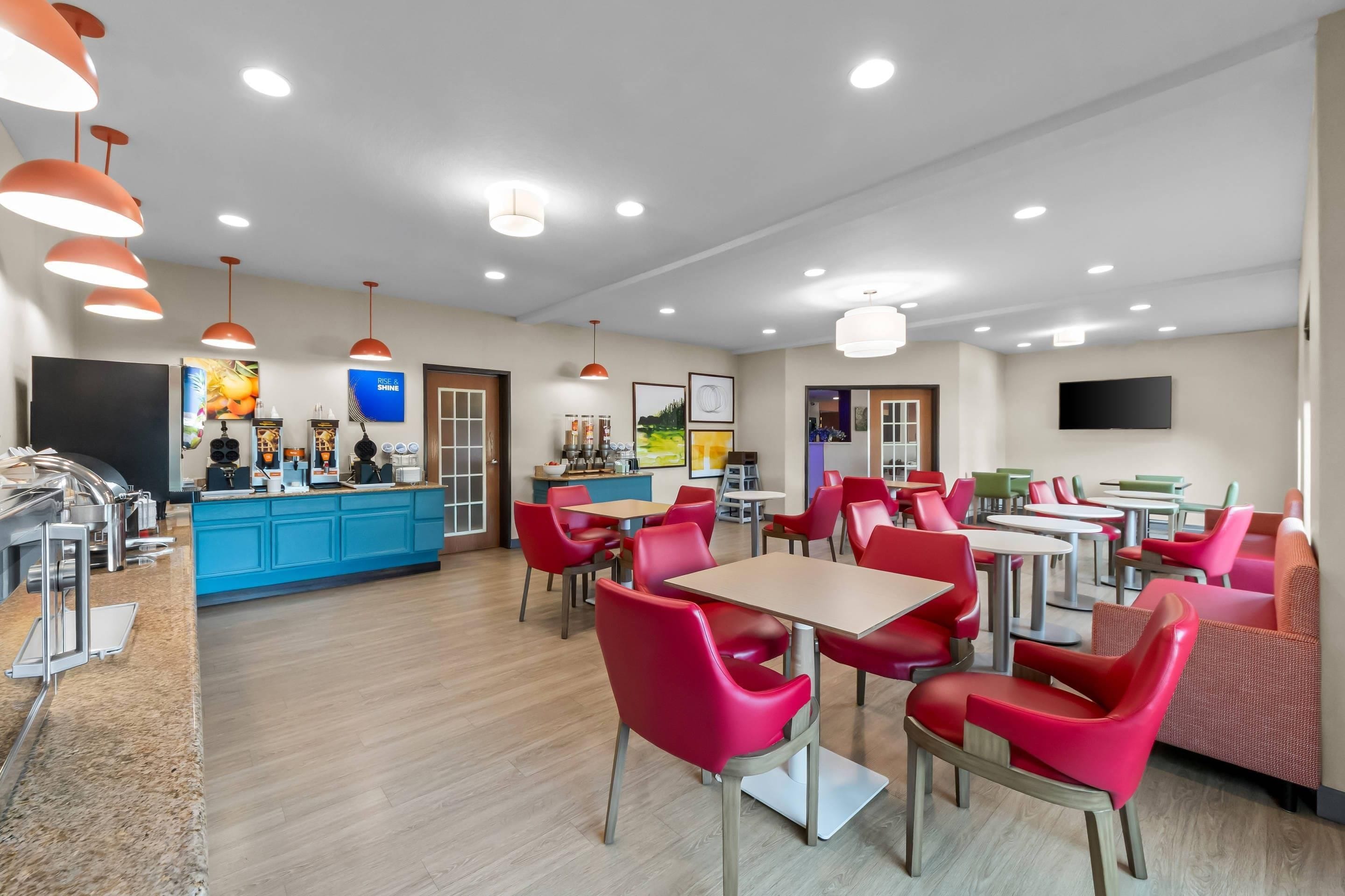 Una cafetería moderna con sillas rojas, mostrador azul y un televisor en la pared.