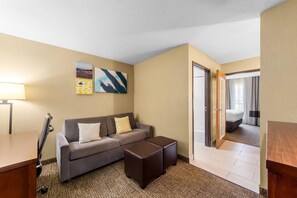 A hotel room with a sofa, ottoman, lamp, and artwork on the wall.