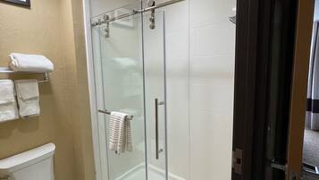 Een moderne badkamer met een douchecabine van glas, een toilet en een handdoekrek met meerdere handdoeken.