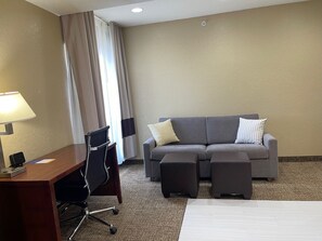 A hotel room with a desk, chair, sofa, ottoman, and a bed.