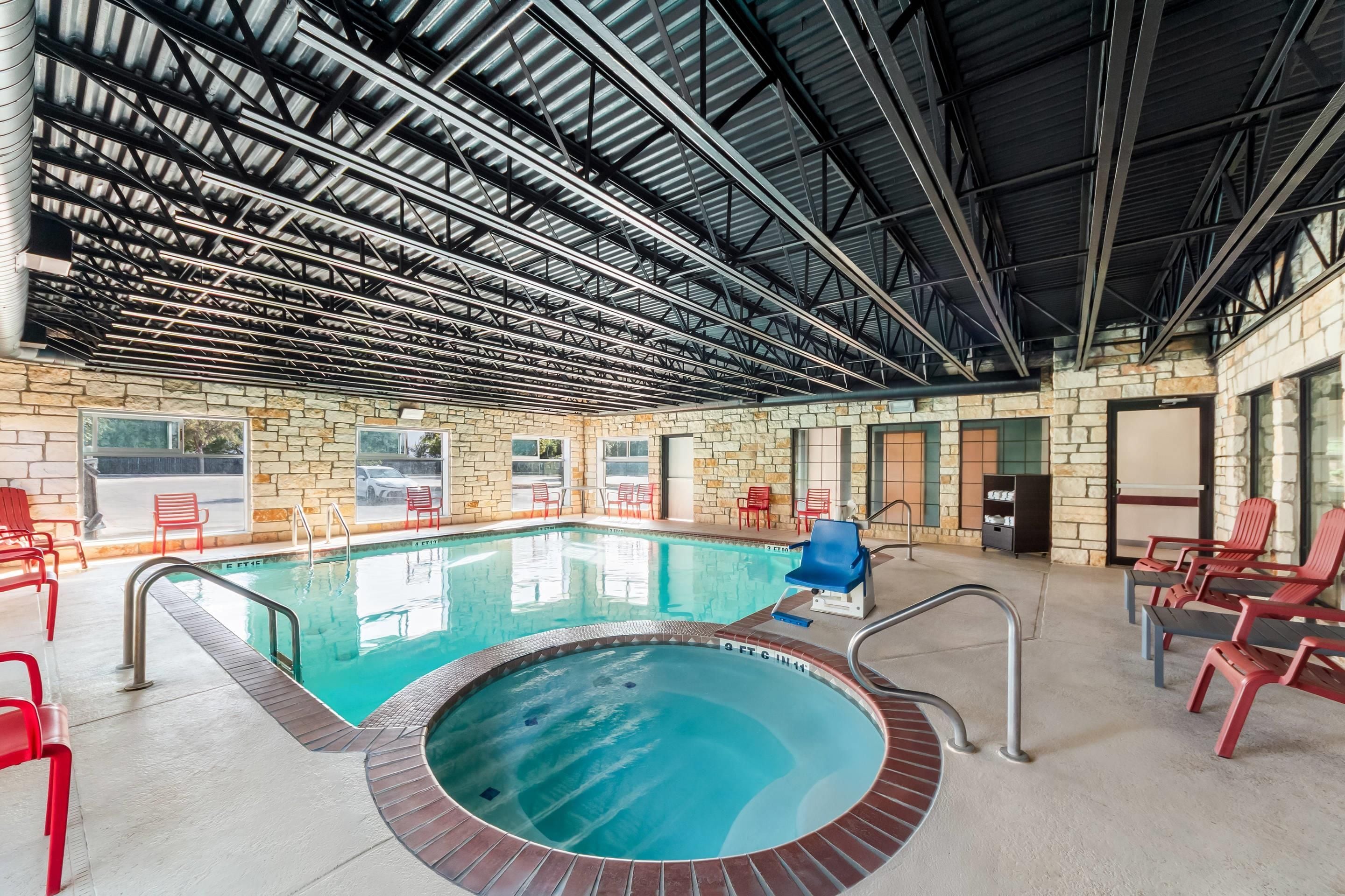 An indoor swimming pool with a stone wall, red chairs, and a metal roof structure.