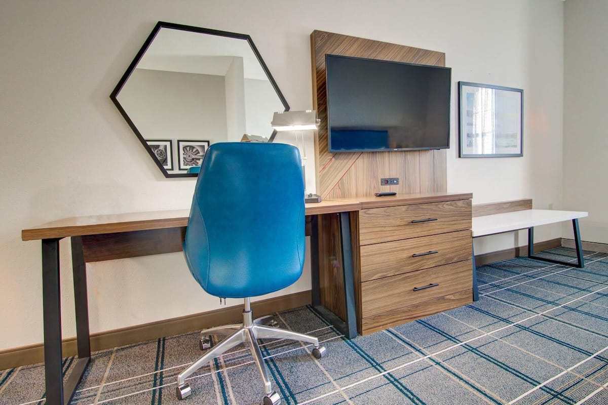 Een hotelkamer met een bureau, stoel, televisie en een spiegel.