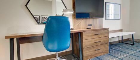 A hotel room with a desk, chair, television, and a mirror.