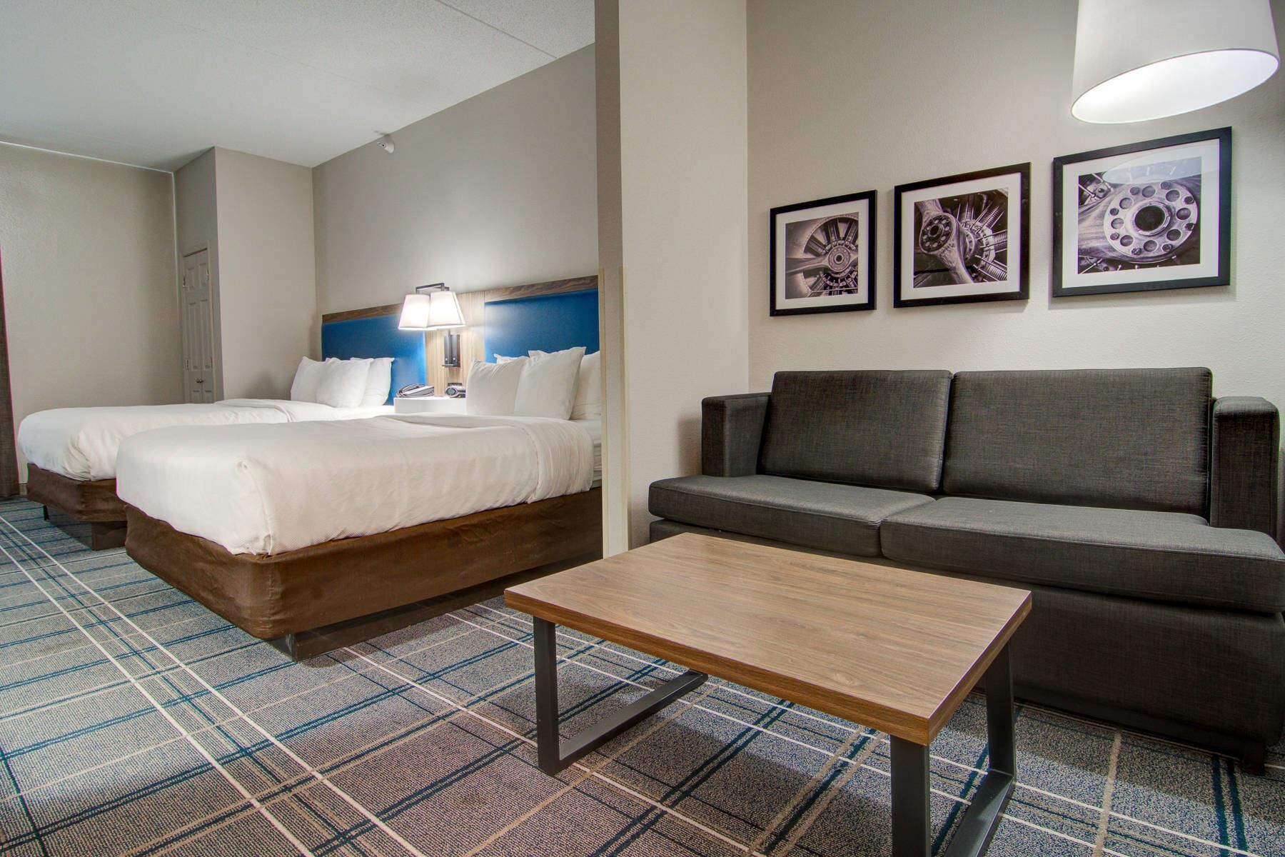 A hotel room with two beds, a sofa, a small table, and three framed pictures on the wall.