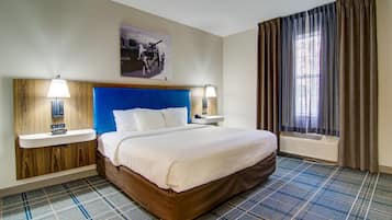 Habitación de hotel con cama, dos mesitas de noche, un reloj de pared, una ventana con cortinas y un aire acondicionado instalado en la pared.