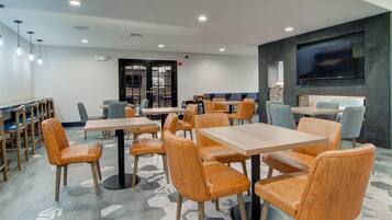 Un restaurant moderne doté d’un sol à motifs hexagonaux, de tables et de chaises en bois, d’un éclairage encastré au plafond et d’un grand téléviseur à écran plat fixé au mur.