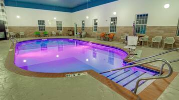 An indoor swimming pool with a blue and purple illuminated edge, surrounded by chairs and a tiled floor.
